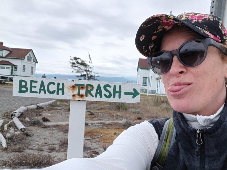 Hiker making a face next to a sign with an arrow for beach trash. Photo by It Sounds Like Camera.