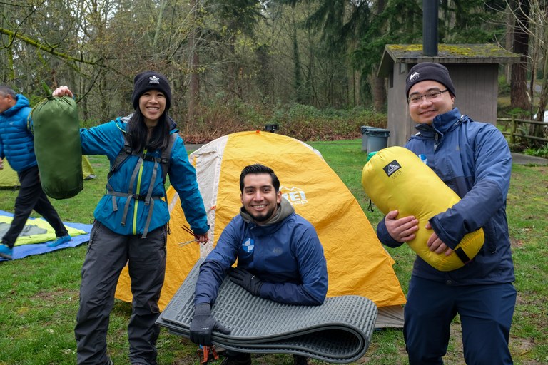 ECOSS Three people holding camping gear smile in front of a tent.