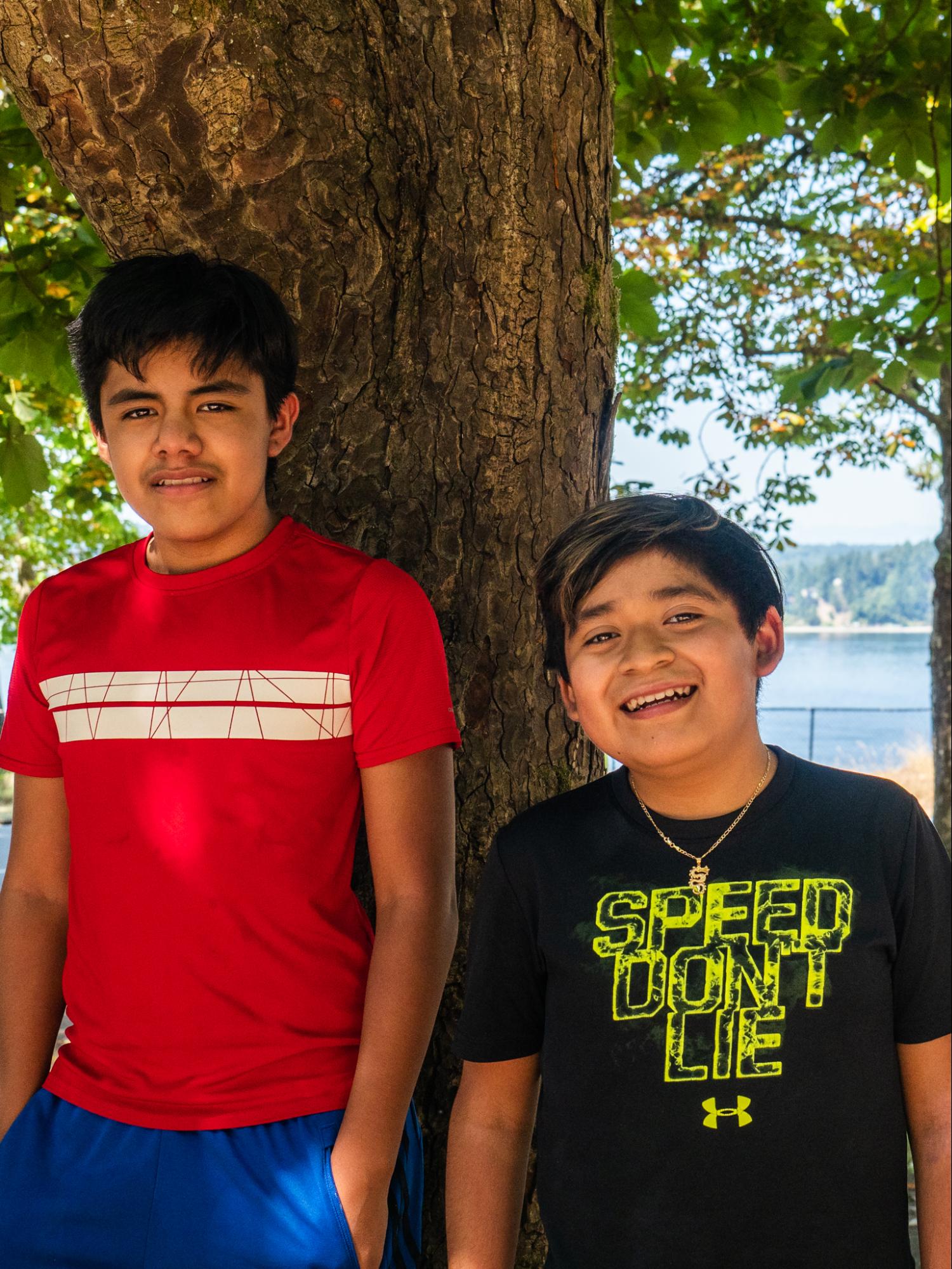 El Centro De La Raza Two students stand in front of a tree and smile at the camera.