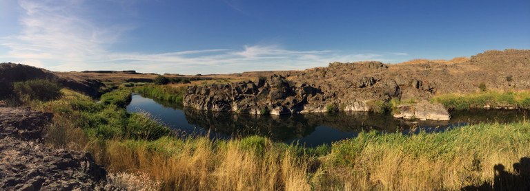 Photo of a river in a landscape of grasses and rock.