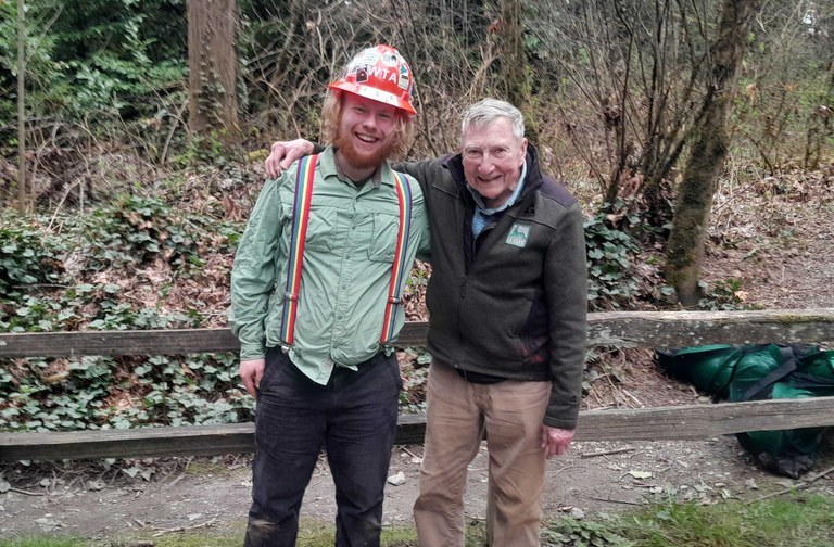 Fern Martin and Pete Dewell stop and smile at Ring Hill Forest Two volunteers smile with their arms around each others shoulders in an open forest