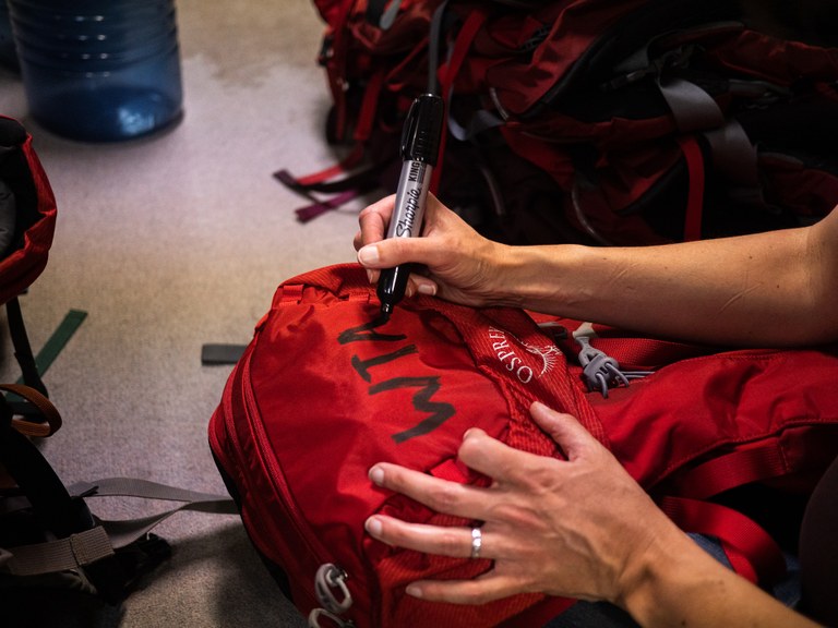 Gear library by Lily Poppen A WTA staff member uses a large, black Sharpie to write WTA on a new, red backpack.