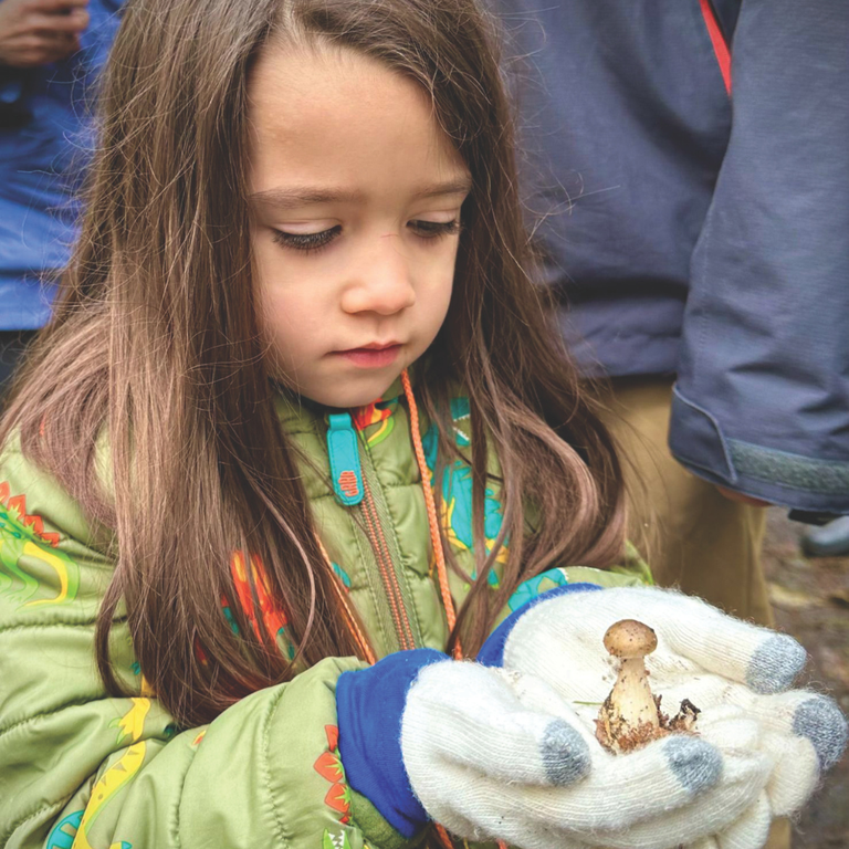 A child holds a mushroom in gloved hands.