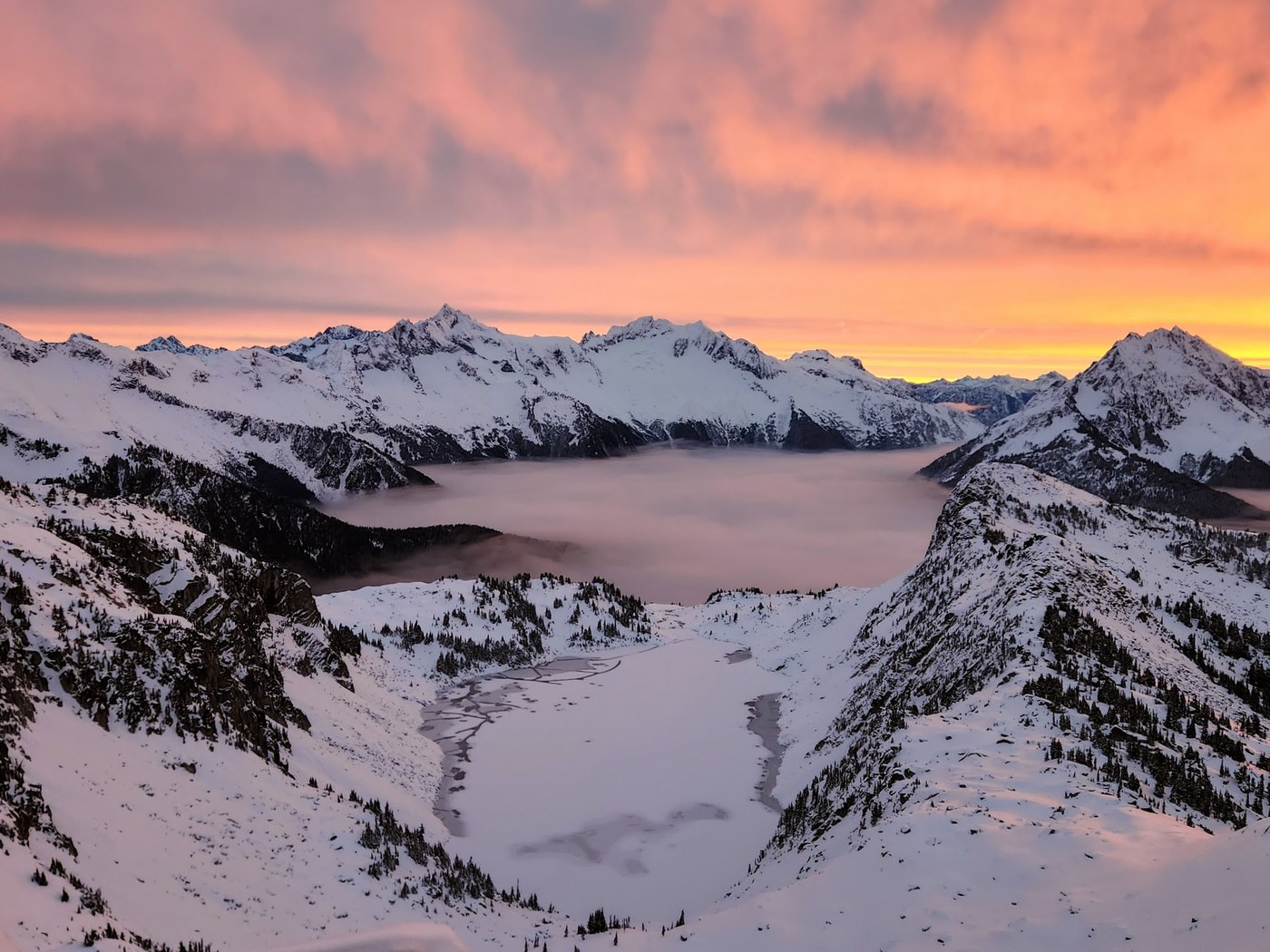 A peach-colored sky above a frozen lake surrounded by snowy peaks