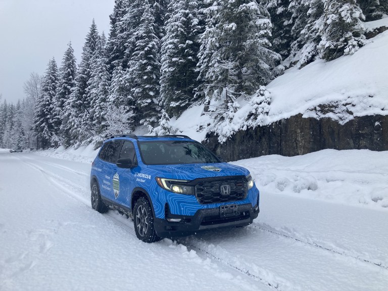 A blue Honda with a WTA logo drives down a snowy forest road. 