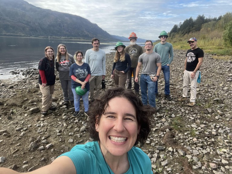 A group of WSU students gather behind Southwest regional coordinator Stasia Honnold for a selfie while standing on the bank of the Columbia River.