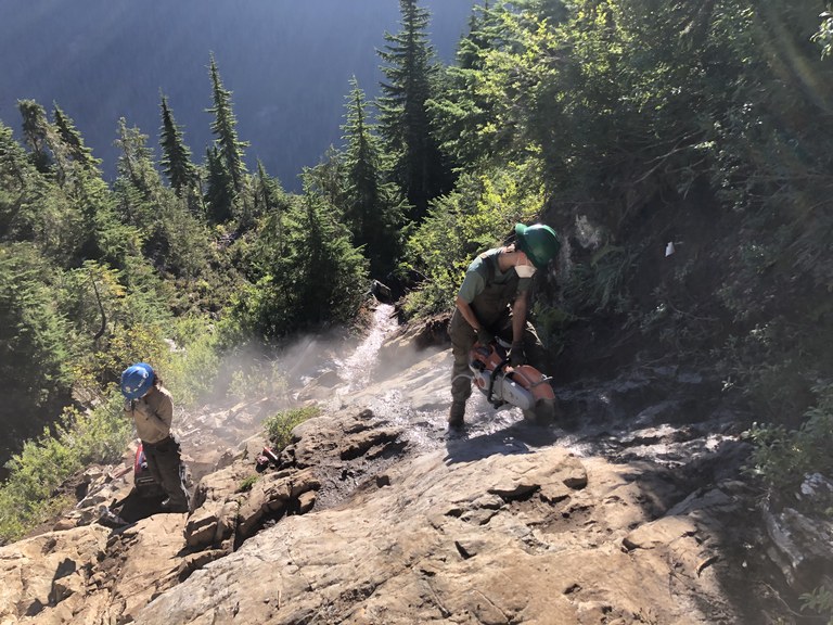 WTA crews use a power tool to cut steps into a rocky trail.