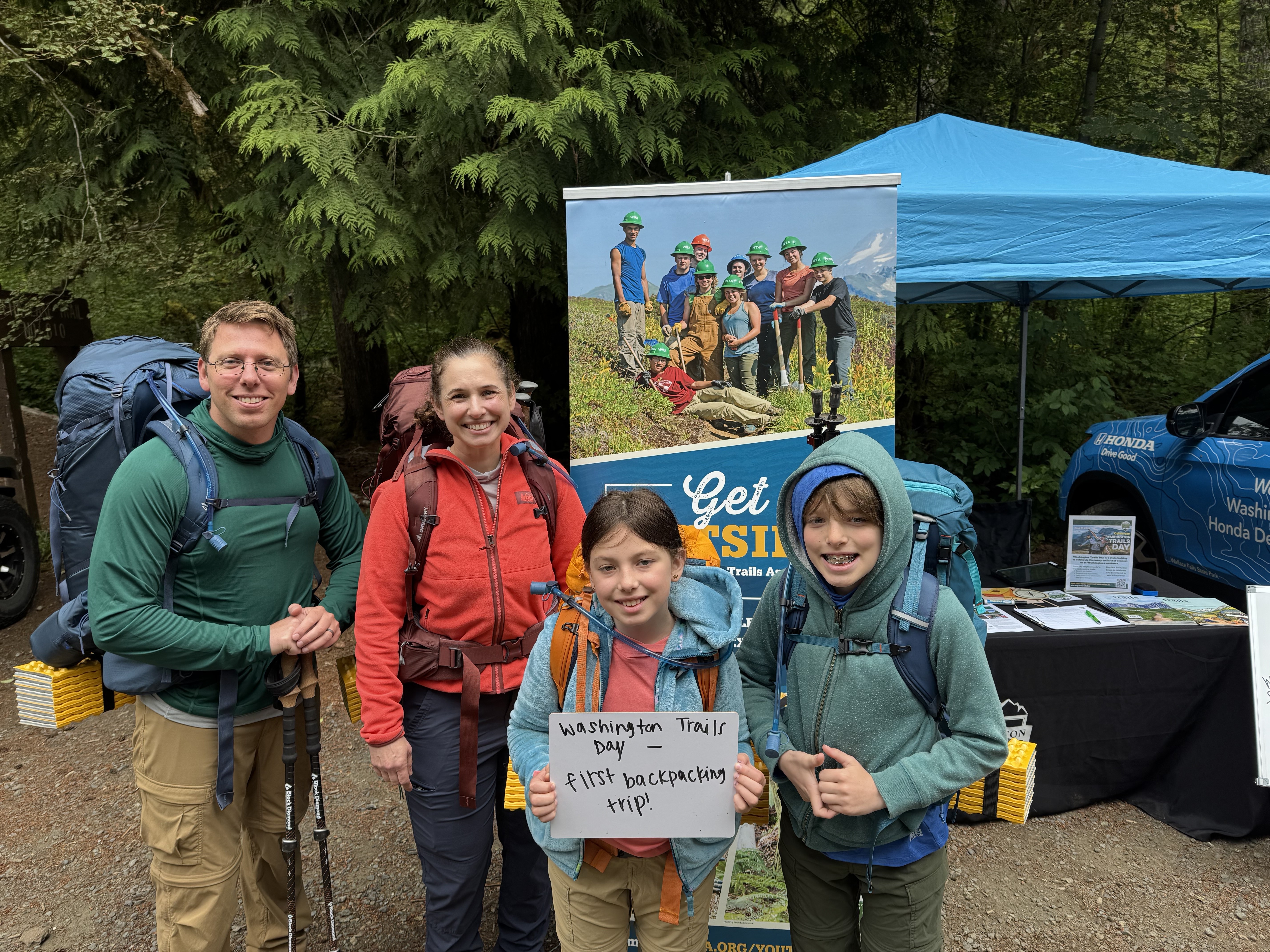 Hiking family holds sign celebrating trails Hiking family holds sign celebrating trails