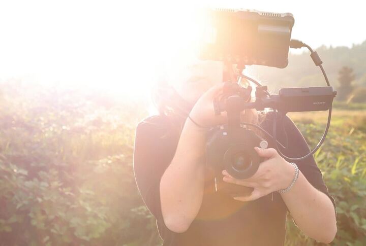 Sun shinning on right side of photo. Woman holding cinema camera. 