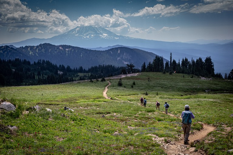 Hikers on a clear trail with snow-capped Mt. Rainier in the distance. 