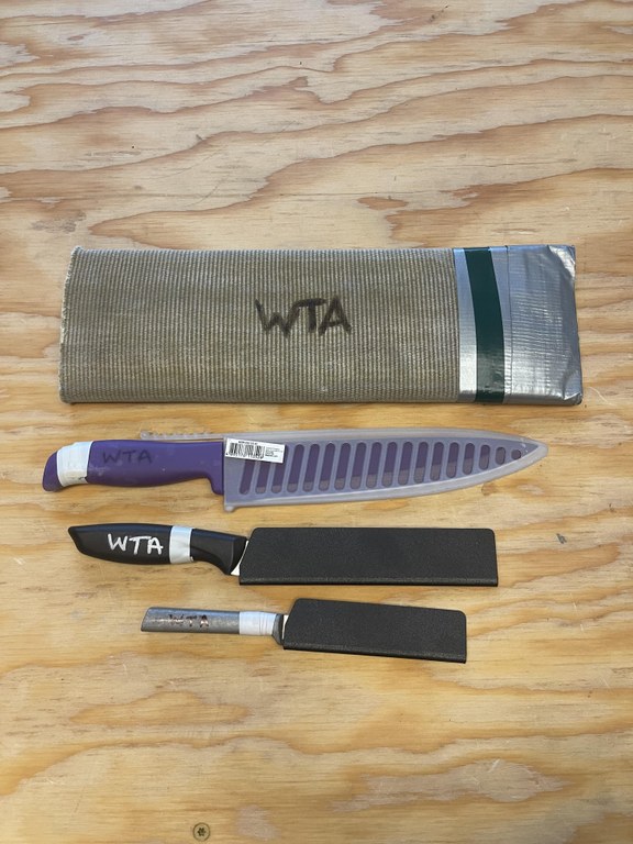 Three knifes are placed next to an old section of fire hose.