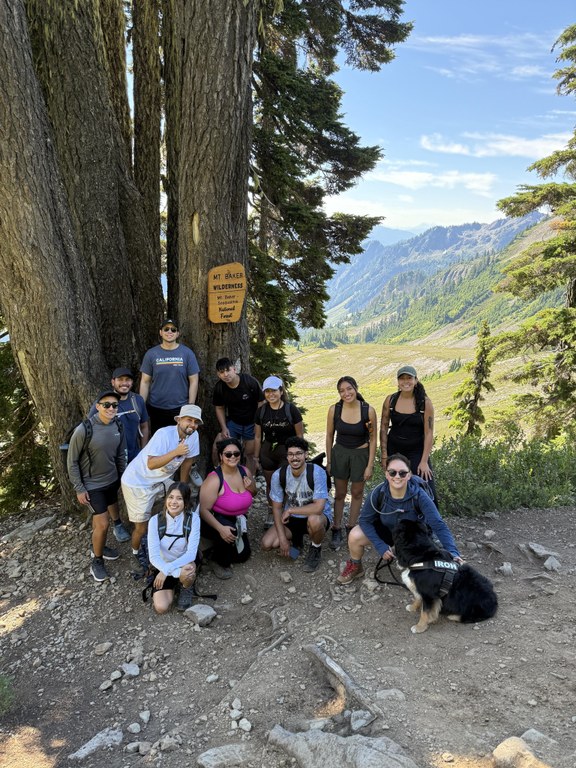 Twelve participants and a dog gather by a forest sign on a hike.