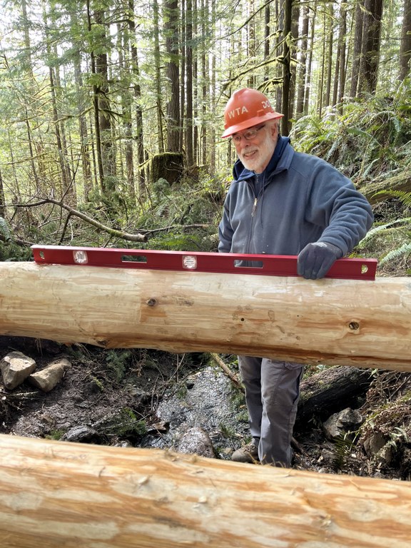 A volunteer holds a level up to the new bridge to ensure it is leveled. 