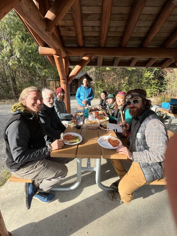 A group of volunteers and trail crew members sit on a picnic bench.