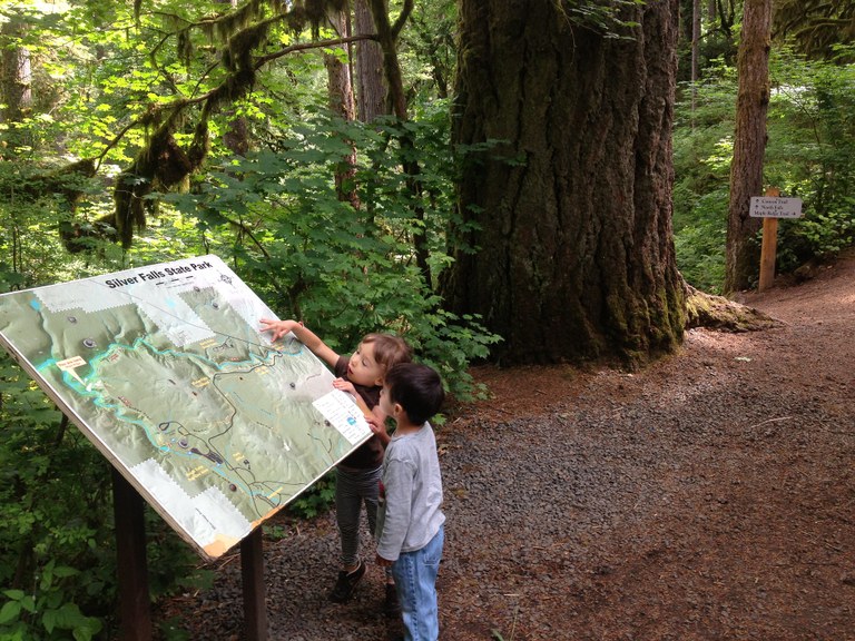 Two small kids touching and looking at an interpretive sign that is much bigger than them.