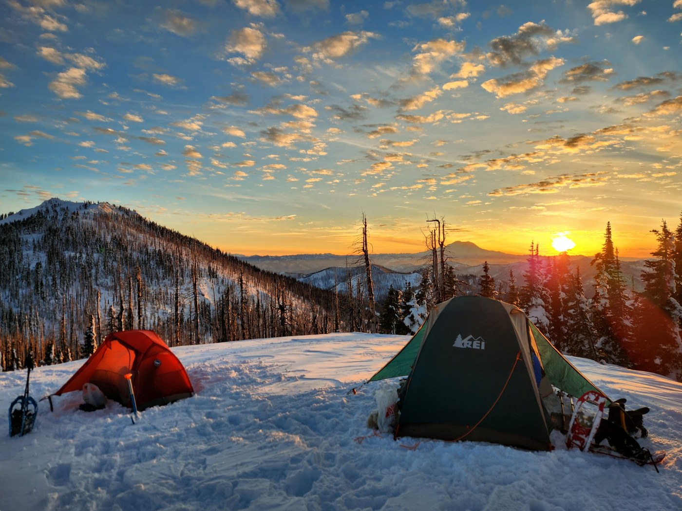 two tents sit on snowy overlook of beautiful mountains at sunrise/set