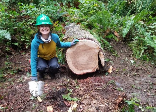 A volunteer smiles next to a newly-cut log. Photo by Robert Canvass