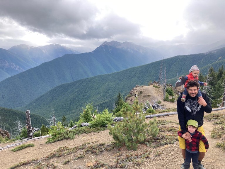 A hiker stands with two kids on a mountain trail. 