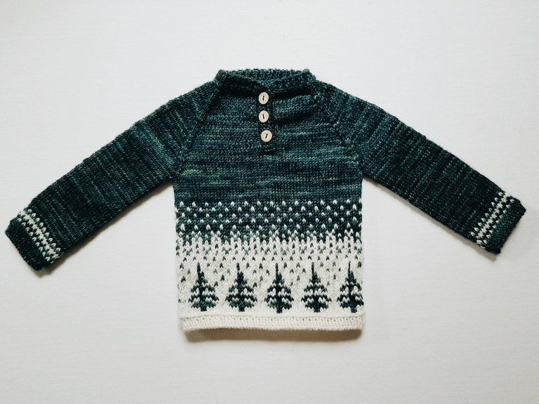 A small knit sweater, fading from green to white, with snow and trees.