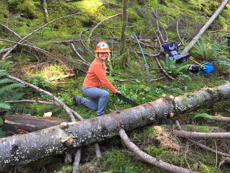 Liz smiles at the camera as she saws through a fallen log.
