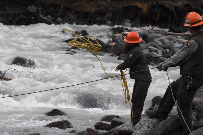 Building a bridge NPS crew members in hard hats use ropes to move the log bridge across the river.