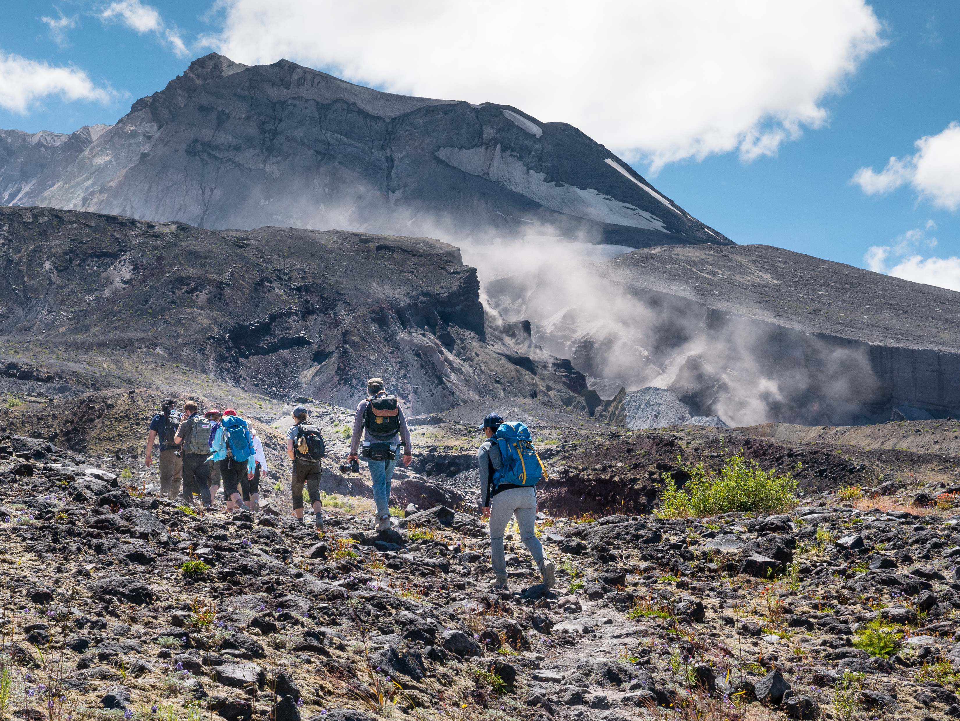 Hikers trek up the Loowit Falls Trail with dramatic mountain in the background and fog rolling in.