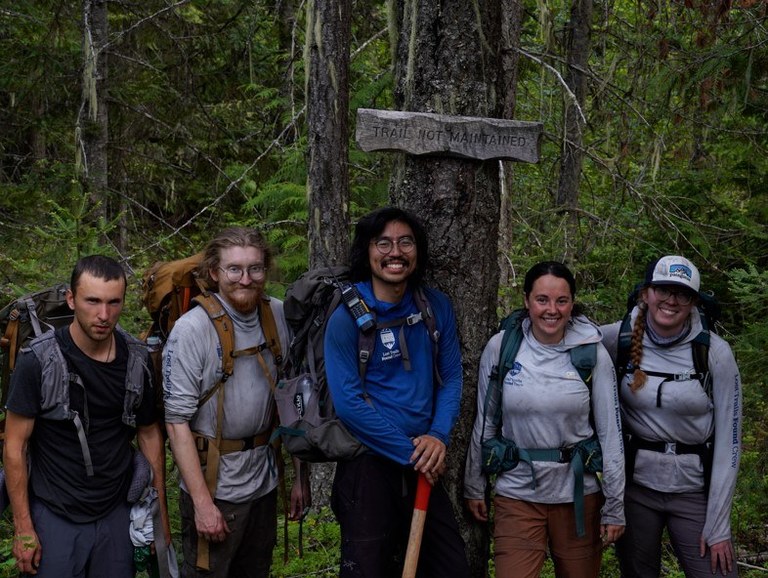 A pro WTA trail crew stands next to a sign that reads "trail not maintained"