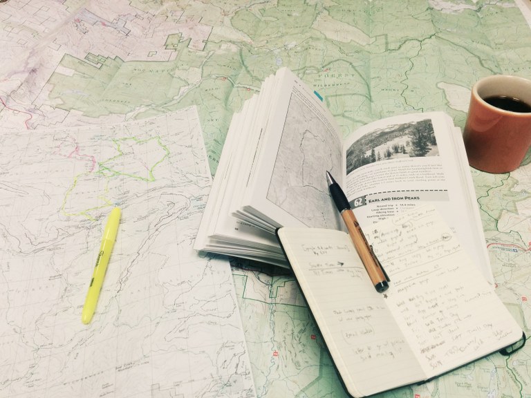 A map with a hiking reference book, notebook, pen, highlighter, and mug of coffee on it. Photo by WTA staffer Loren Drummond. 