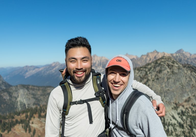 Two hikers put their arms around each other and smile big. 