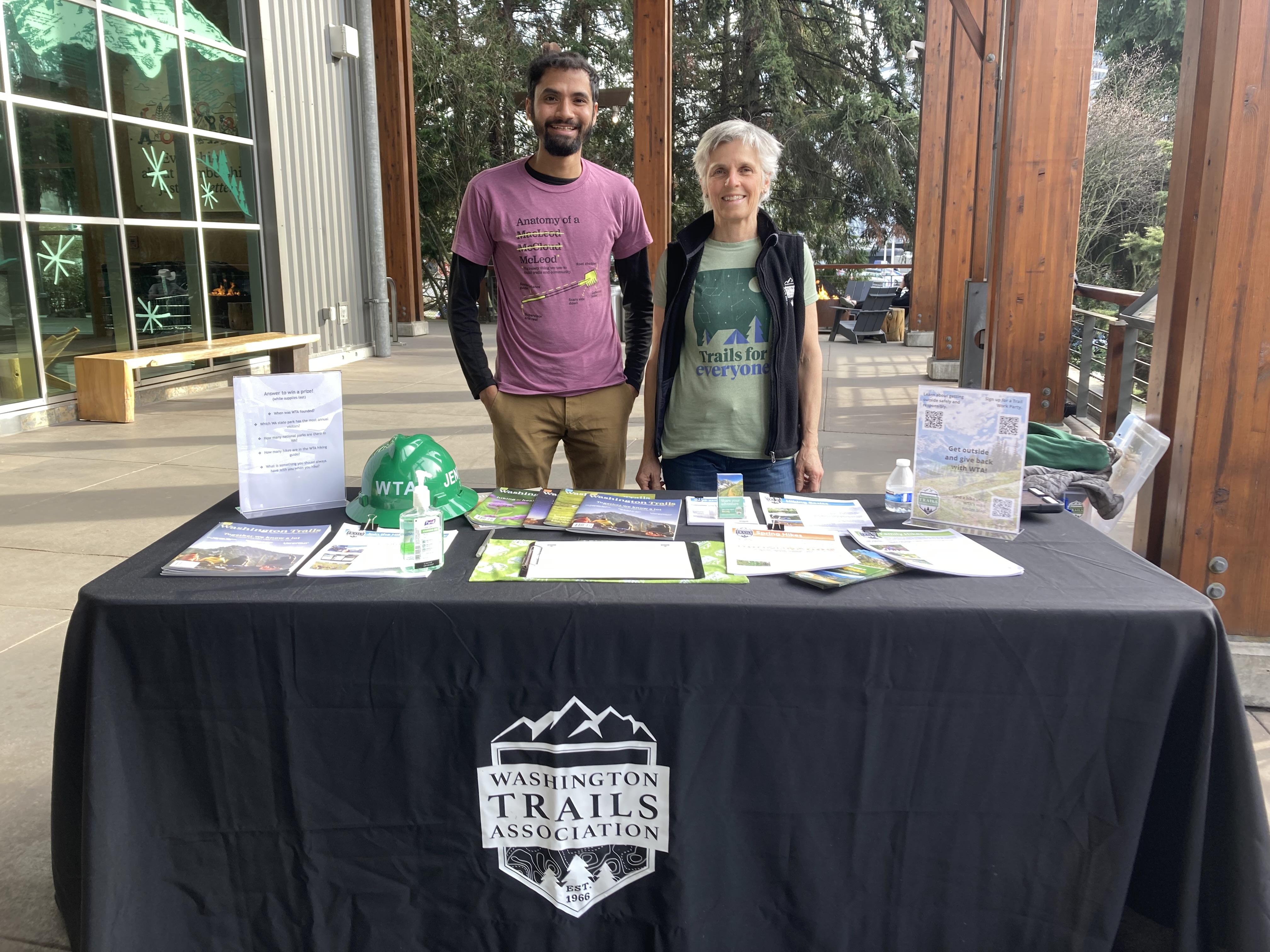 Two volunteer ambassadors pose behind a WTA outreach table outside of REI in Seattle