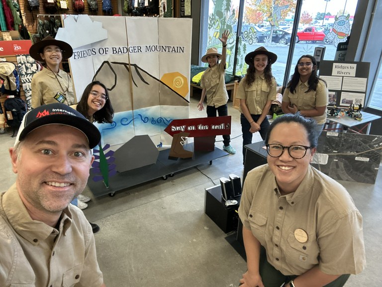 6 kids and 2 adults in front of an interactive display about trails. 