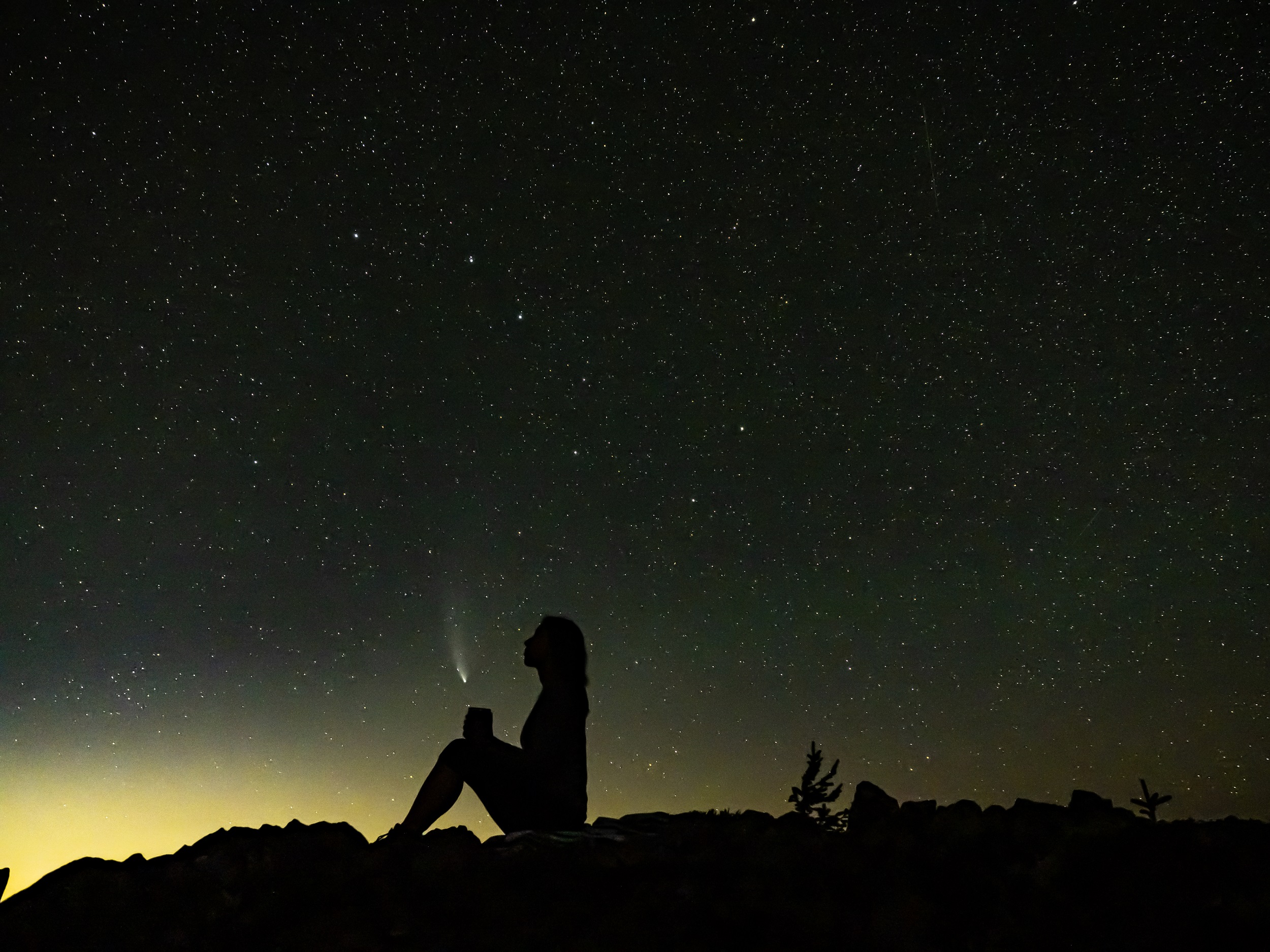 Photo by Michael Margoshes Hiker holding cup on mountain with comet at night