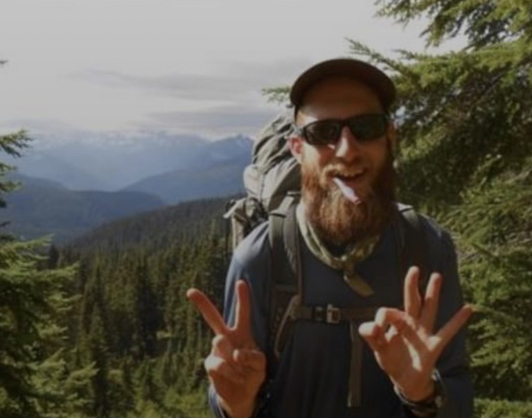 A hiker smiling at the camera with a toothbrush in their mouth. Photo by Michael DeCramer.