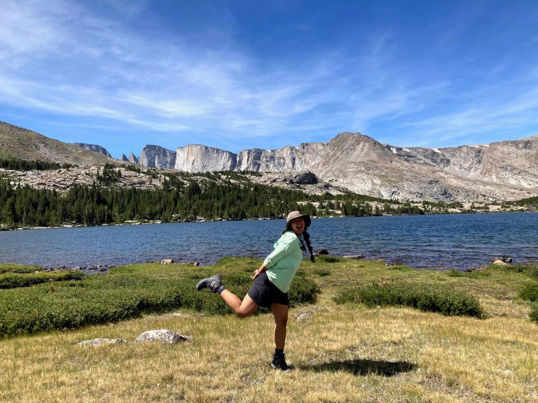 A hiker makes a fun pose in front of the water while smiling at the camera. Photo by MJ Mahan.