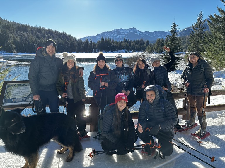 A group of snowshoers smile on a bridge on a sunny day.