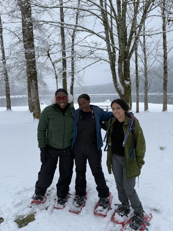 Three snowshoers pose for a photo in front of a lake. 
