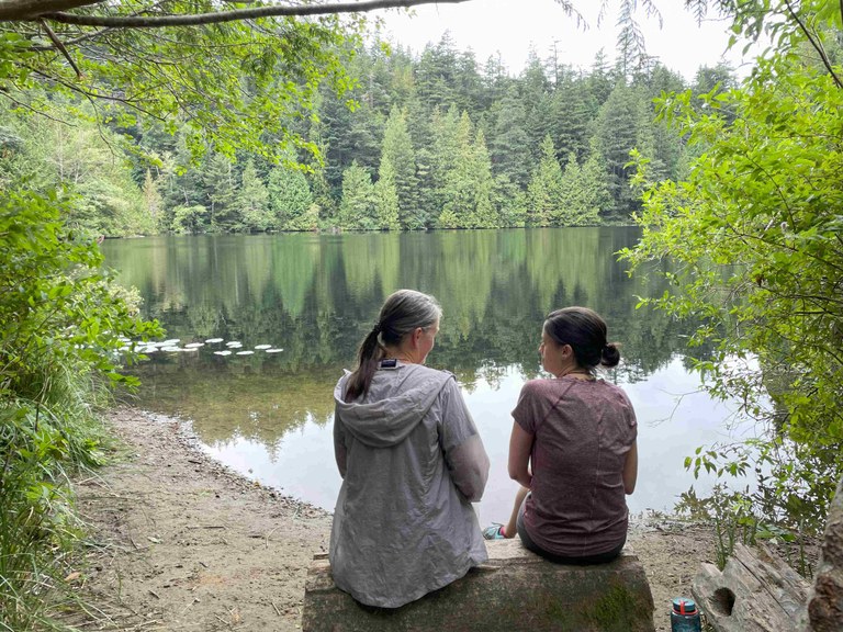 Nicole and her mother sitting on a log at a lake. Photo by Nicole Masih-Théberge. 