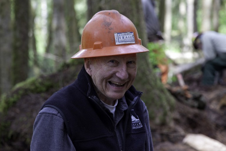 Pete Dewell smiles big on a break during a work party in a forest. 
