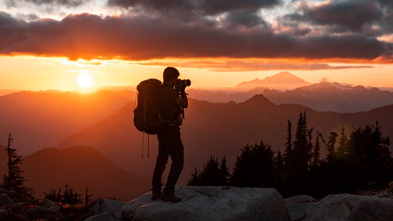 A photographer takes a picture of a mountain sunset. 