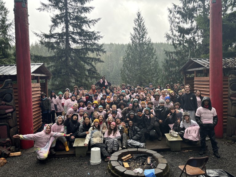 A large group of high school students behind a campfire ring. 