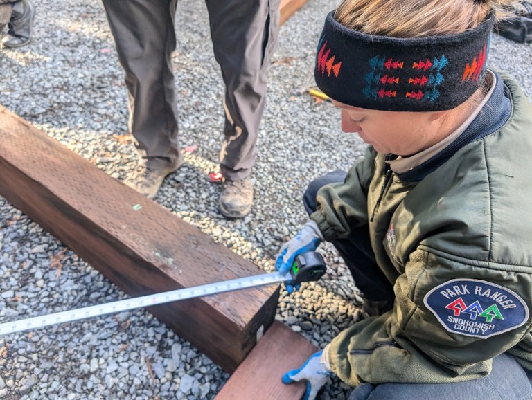 A park ranger measures large beams of wood.