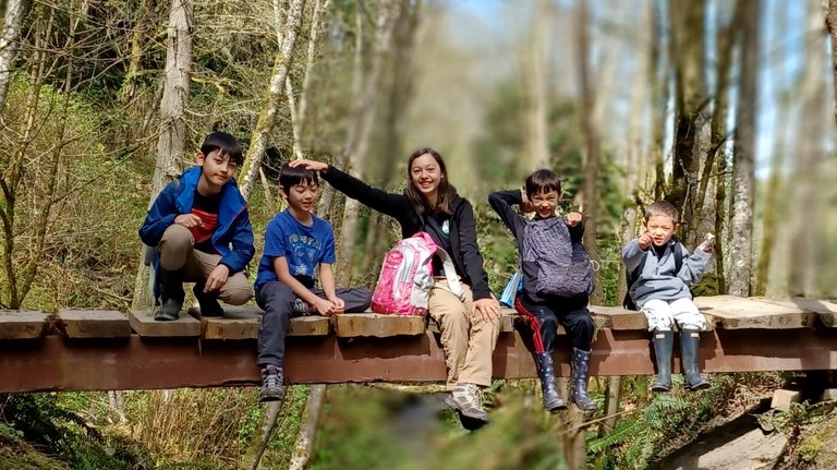 Five kids sit on a wooden bridge together. 
