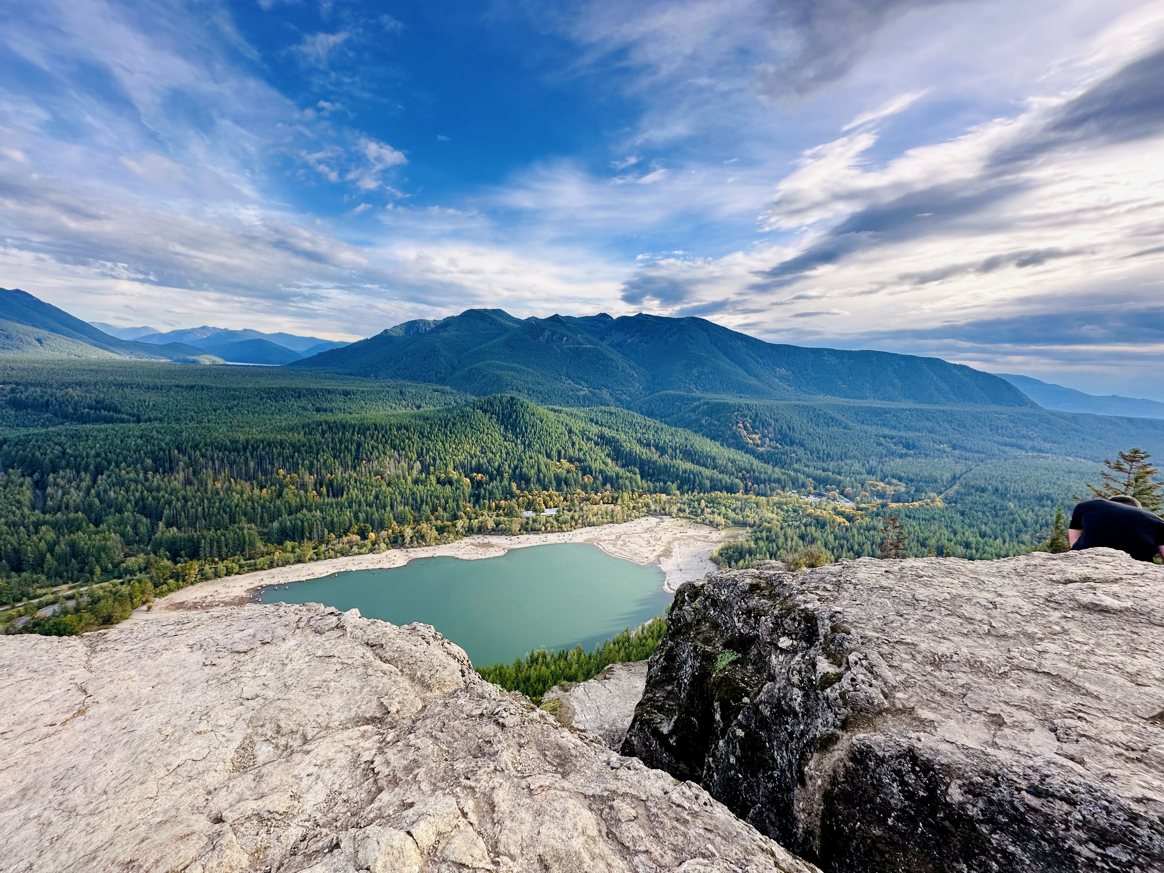 A rocky ledge overlooks an aqua lake surrounded by green mountains
