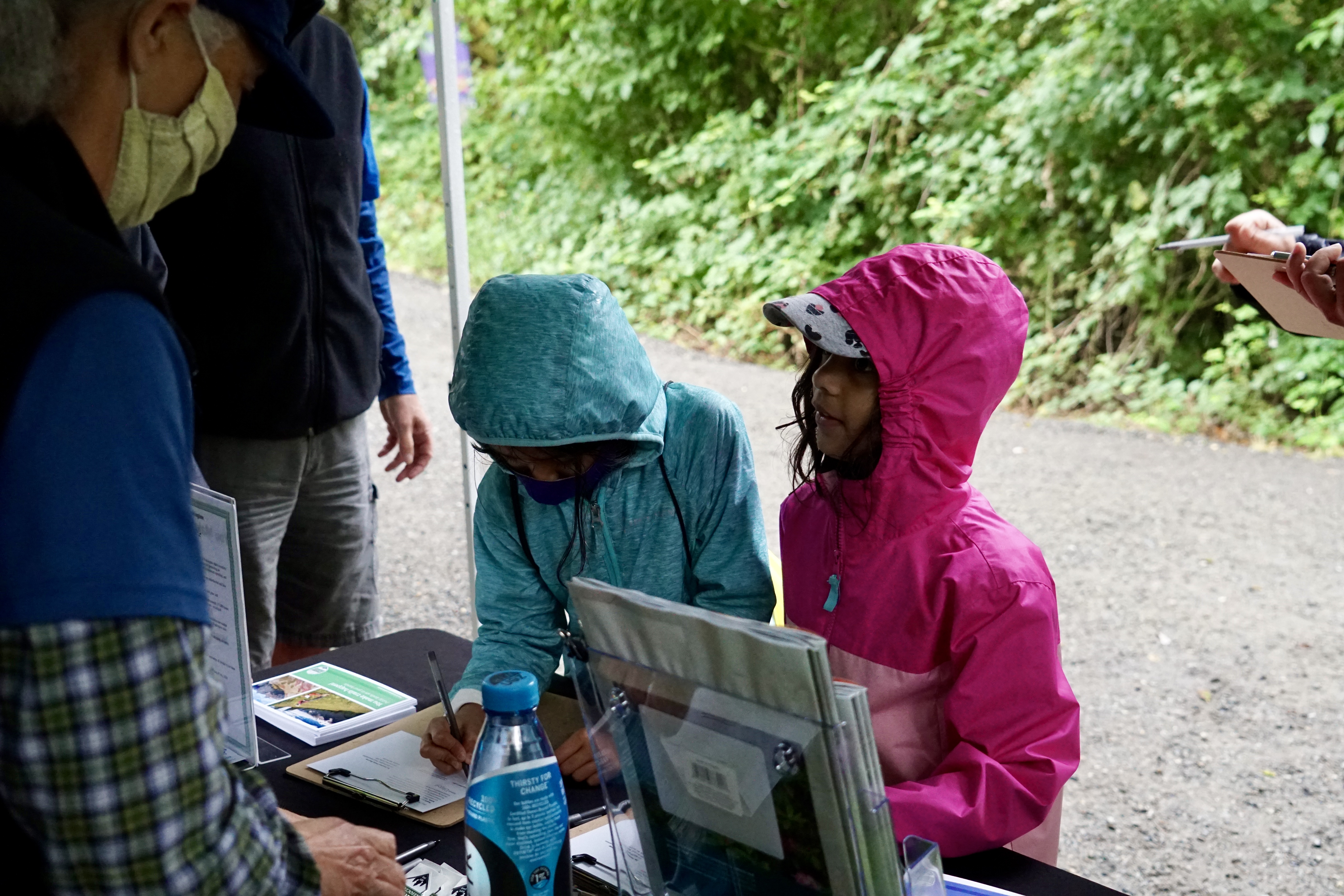 Two young children wearing rain jackets sign postcards in support of trails.