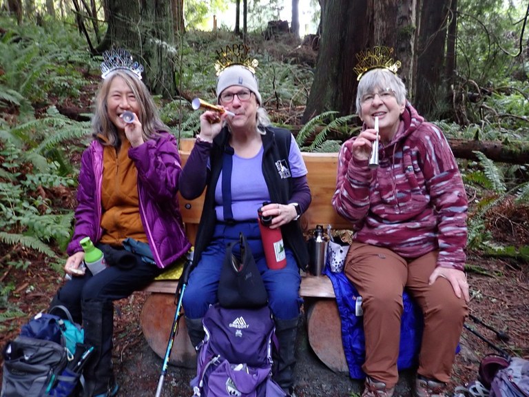 three hikers sit on bench on trail wearing hats and whistles to ring in the new year!