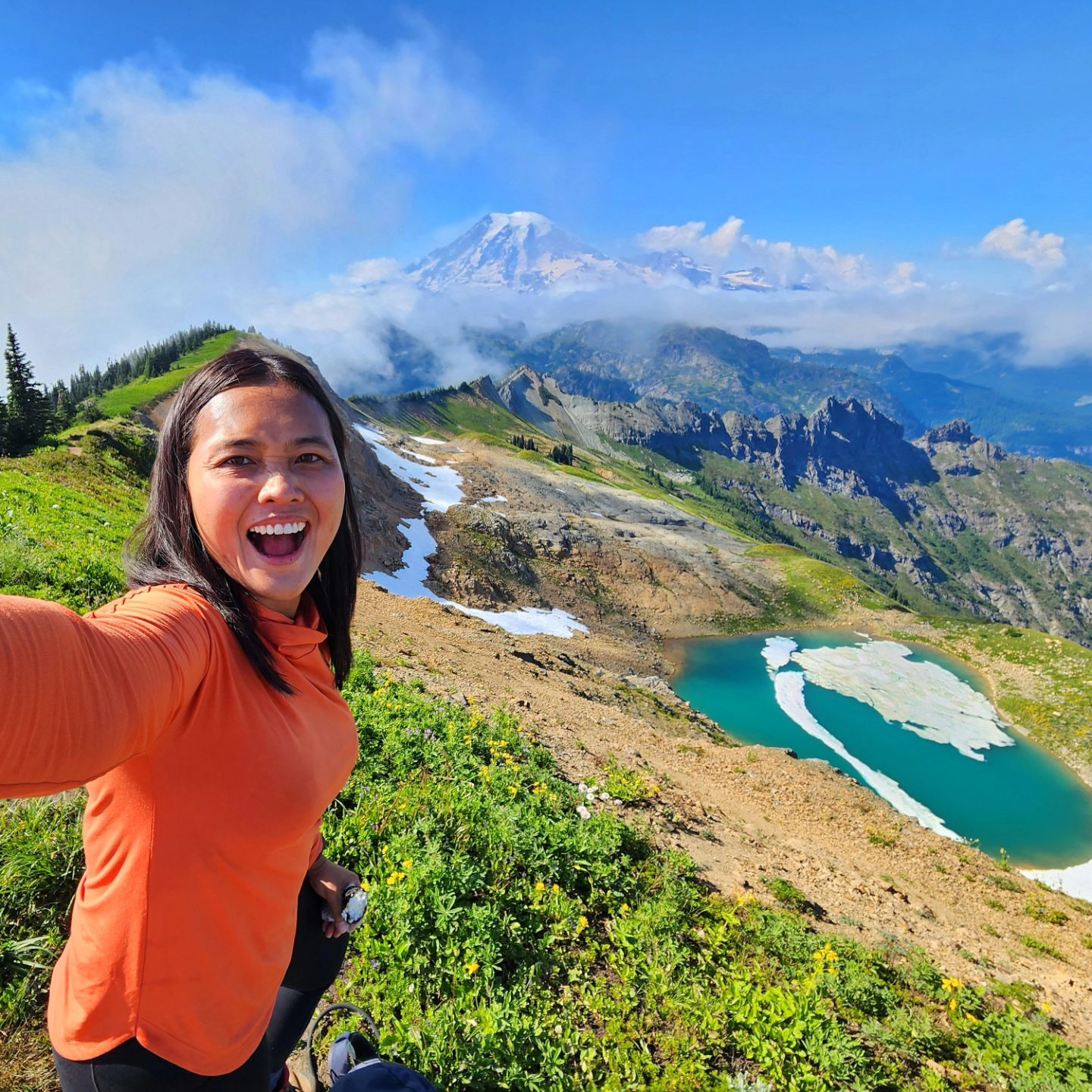 Women smiling taking a selfie with mountains and alpine lake in background.