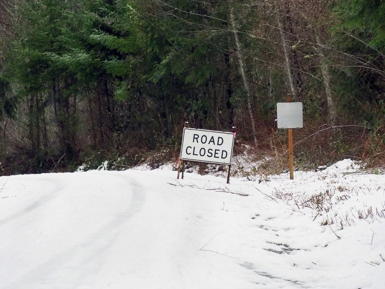 A snow-covered forest road with a road closed sign. 