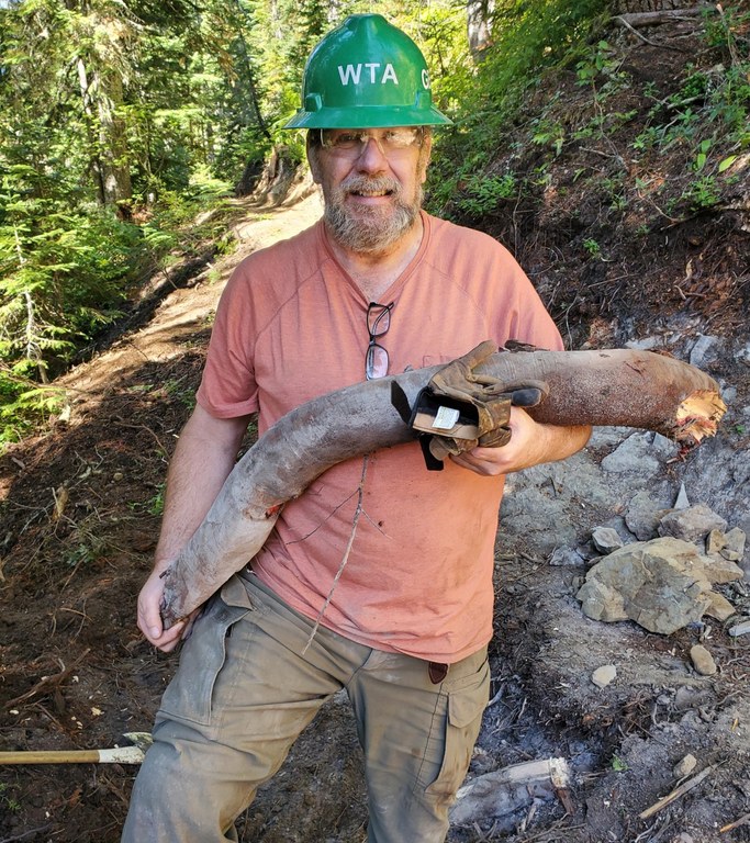 A volunteer stands holding a root he removed from the trail bed. Photo by George Peppin. 