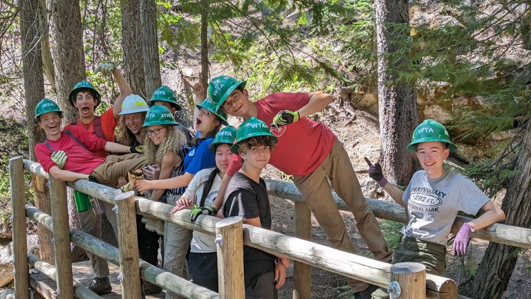 A group of teens laugh on a wooden trail bridge. 