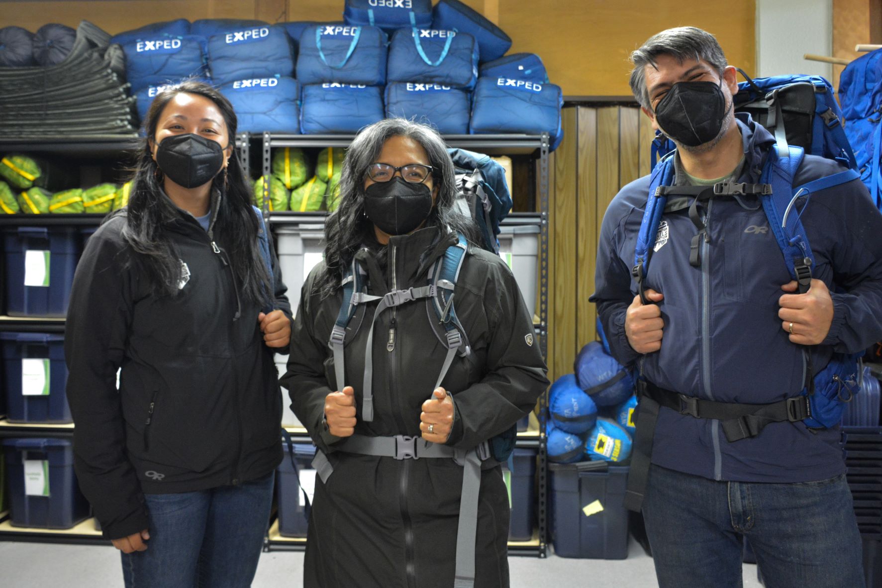 Two Washington Trails Association staff and Representative Strickland stand next to each other, masks on, at the WTA gear library.